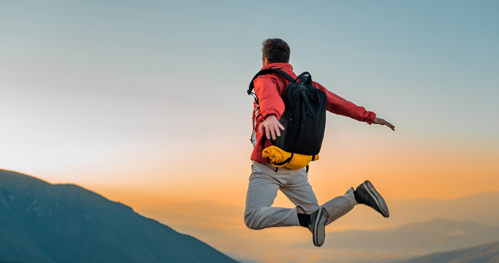 A happy man traveler with outstretched arms air jumping on the mountain top. Adventure travel. concept of success free freedom.