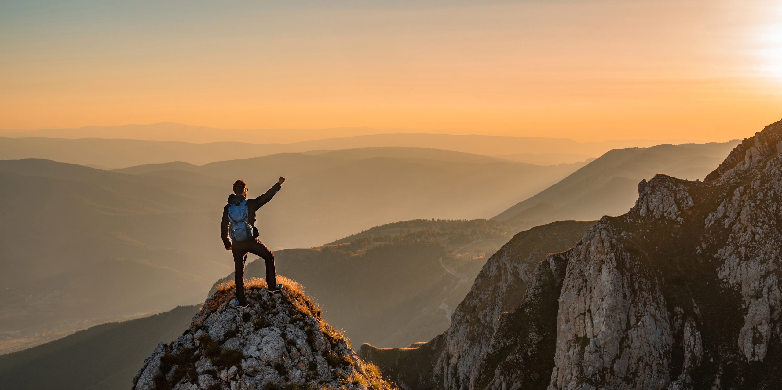 A happy man hikers standing with arms up on the mountain top celebrates successful completed hiking route adventure travel.
